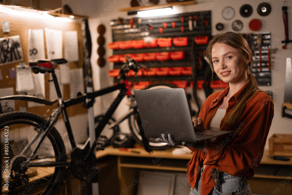 Female mechanic in her Workshop or garage looking at laptop. Bike shop owner with laptop