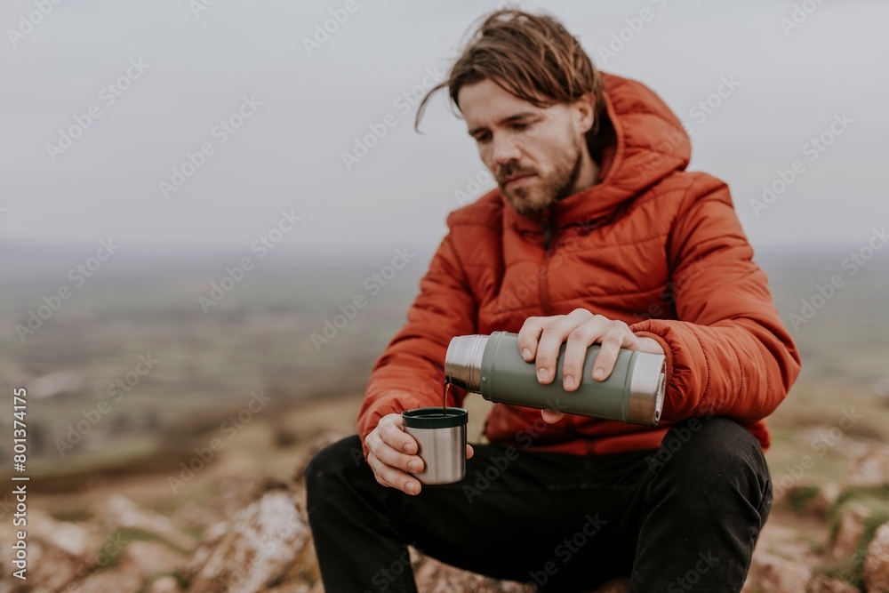 Fototapeta premium Drinking coffee from a thermos, while hiking