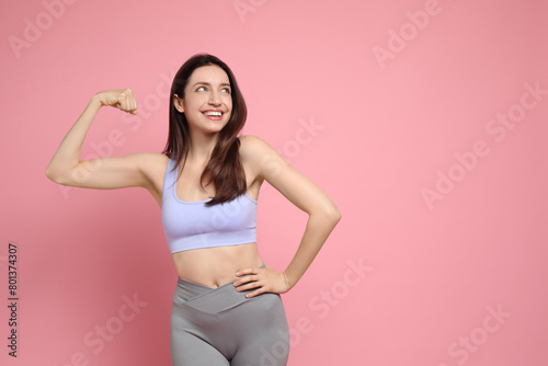 Happy young woman with slim body showing her muscles on pink background, space for text