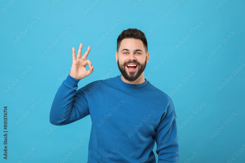 Happy young man with mustache showing OK gesture on light blue background Happy young man with mustache showing OK gesture on light blue background