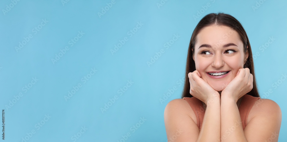 Smiling woman with braces on light blue background. Banner design with space for text Smiling woman with braces on light blue background. Banner design with space for text