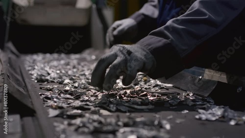 Worker sorts trash on conveyor belt at waste recycling plant. Metal pieces falling into a box from recycling processing machine. Man sorts pieces of metal, iron or steel with his hands