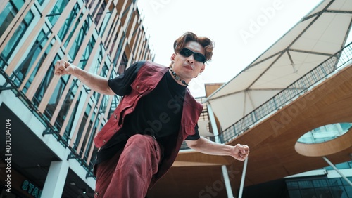 Low angle of asian attractive hipster pose at camera surround by mall. Portrait of break dance choreographer looking at camera while dancing in hip hop style. Outdoor sport 2024. Endeavor.