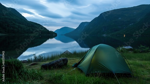 Tent by the lake in a beautiful landscape, evening time. Camping scene with tent on beautiful mountains and lake. Golden sunrise illuminating tent camping dramatic mountain landscape.