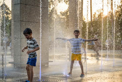 Boys jumping in water fountains. Children playing with a city fountain on hot summer day. Happy friends having fun in fountain. Summer weather. Friendship, lifestyle and vacation