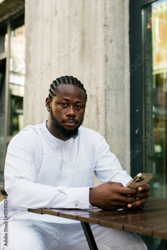 African American hipster guy in cultural and ethnic clothing dashiki chatting on smartphone outdoors, texting with friends on social networks. Millennial generation and Internet blog concept