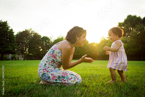 Young mother and daughter playing outdoors on the grass in nature on a summer sunset .concept of harmony in maternity and motherhood, sharing quality time together.
