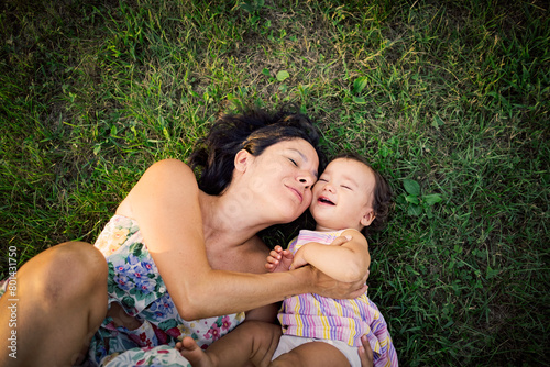 Young mother and baby daughter laying together on the grass in nature enjoying quality time together .concept of harmony in maternity and motherhood, sharing happy moments together.