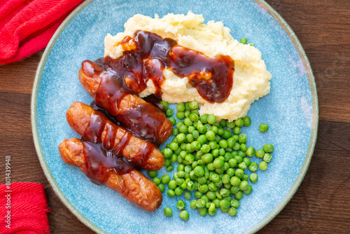 sausages, mash and gravy with peas on a turquoise plate