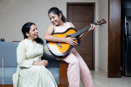 Young Teen Girl with Mother and home playing Guitar and mother enjoying the moment at home sitting at sofa in living room ,Mother and Daughter Relationship Bonding