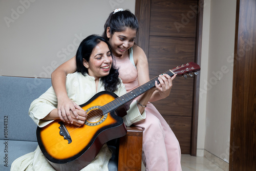 Indian Young Teenage Daughter Helping mother with Guitar Playing at home sitting on sofa, Mother Daughters Relation ship