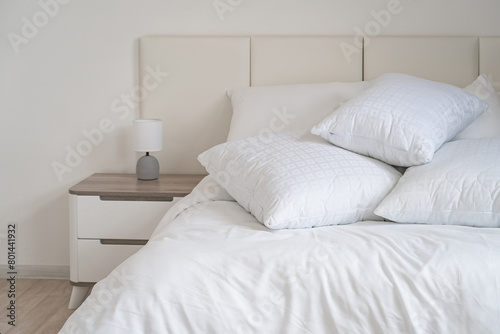 A bed with white pillows and a blanket  next to a bedside table with a lamp  daylight