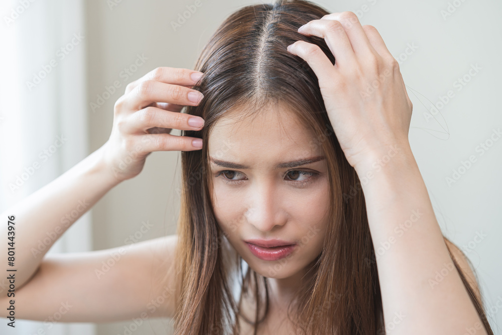 Fototapeta premium Damaged hair symptom, problem hair fall asian young woman, girl worry about balding, looking at scalp in mirror, hand in break into front hair loss, thin problem. Health care treatment for beauty.