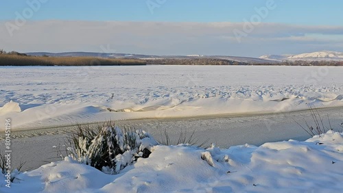 Fairy tale winter scene - a partially frozen water channel surrounded by freshly fallen snow in the soft glow of the winter sun in the distance with the protected landscape of the area called Pálava photo