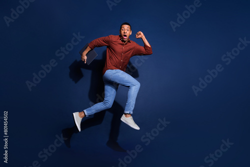 Full length photo of attractive funny guy wear formal shirt jumping high hurrying emtpy space isolated blue color background © deagreez