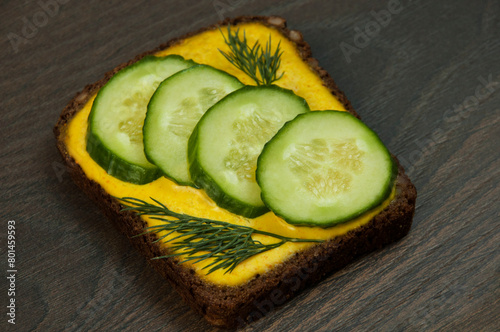 a sandwich with cucumbers and yellow sauce on a wooden background. an appetizing vegetable sandwich on a dark background  © Григорий Юник
