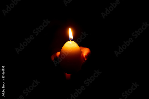 A yellow candle in the shape of an egg in a girl s hand in the dark, Easter