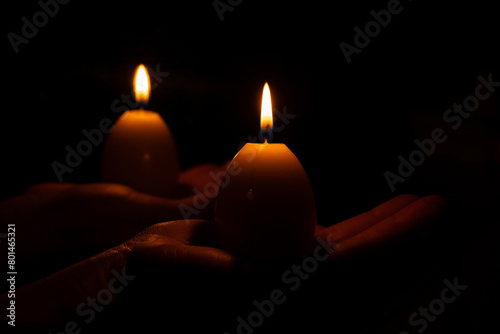 A yellow candle in the shape of an egg in a girl s hand in the dark, Easter