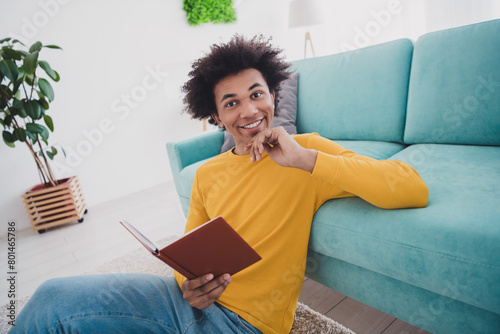 Photo of nice young man sit floor read book think wear yellow pullover white interior apartment indoors