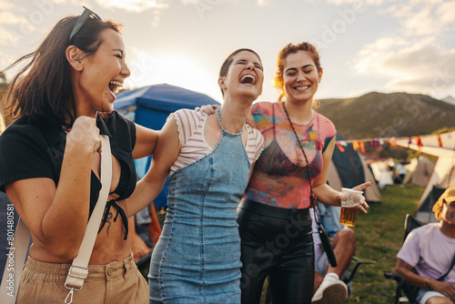 Three female friends embrace, laugh, and celebrate the magic of the summer music festival photo