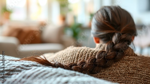  A woman sits on a couch with her back facing the camera, her hair tied in a low ponytail