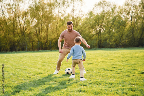 Playing soccer. Happy father with son are having fun on the field at summertime