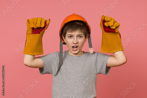 The concept of a rallying or striking construction worker or a boy in a builder's costume with his hands raised upstairs clenched into a fist © Sergey