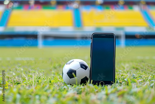 Mobile phone with soccer ball on green grass and blurred football stadium background