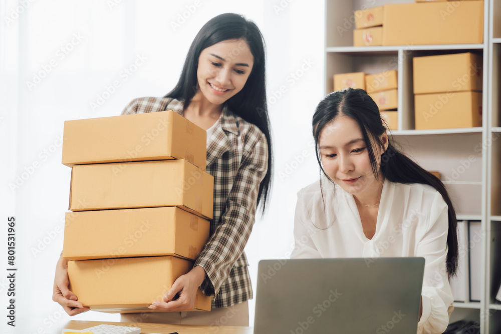 Asian businesswoman using laptop computer checking customer's shipping box online at home. SME startup. Small business entrepreneur, freelancer. Online business, SME work Asian businesswoman using laptop computer checking customer's shipping box online at home. SME startup. Small business entrepreneur, freelancer. Online business, SME work