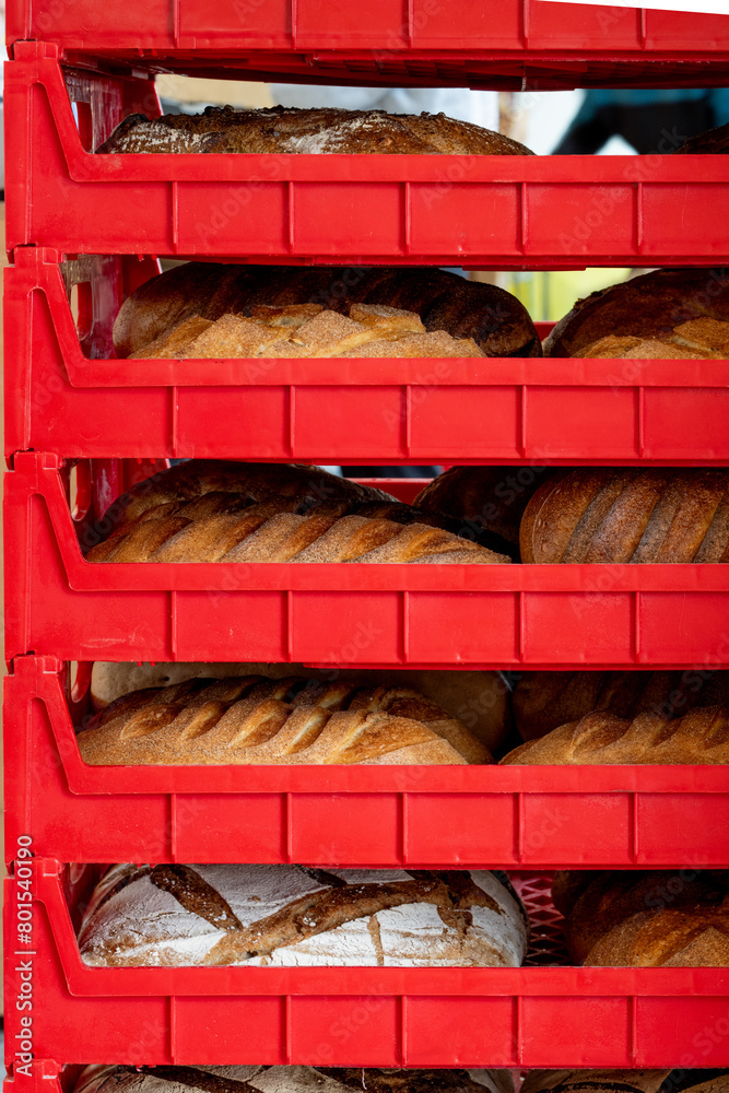 Multiple red plastic trays filled with fresh French bread, buns, and baguettes. The bakery storage racks are for transporting large quantities of supermarket long brown crusty loaves to shelves. 