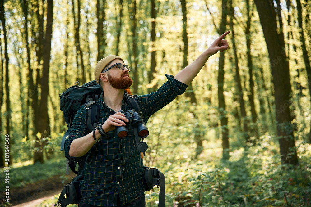 Tourist with binoculars. Bearded man is in the forest at daytime