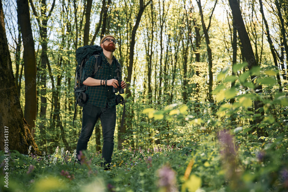 Tourist with binoculars. Bearded man is in the forest at daytime Tourist with binoculars. Bearded man is in the forest at daytime