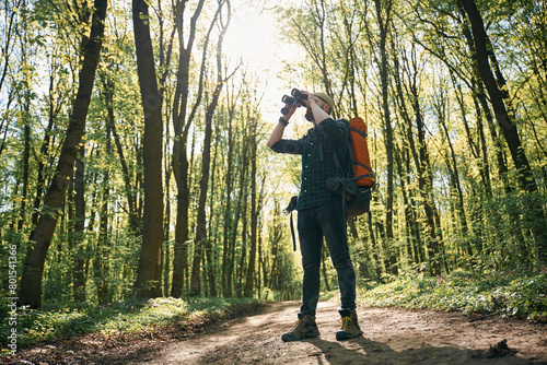 Looking far away by using binoculars. Bearded man is in the forest at daytime © standret