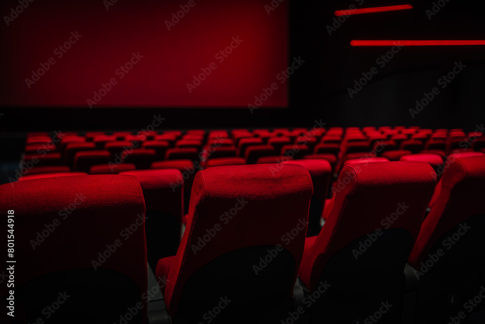 Dimly lit interior of a movie theater with rows of empty red seats facing a red screen, creating a moody, cinematic atmosphere. Dimly lit interior of a movie theater with rows of empty red seats facing a red screen, creating a moody, cinematic atmosphere.