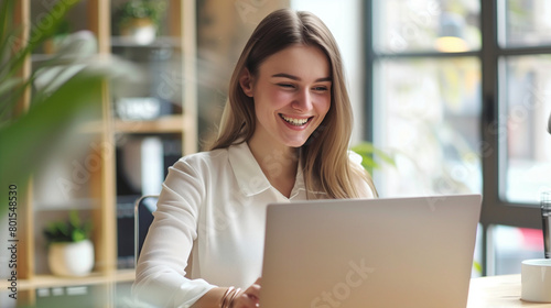 Young happy professional business woman worker employee sitting at desk working on laptop in corporate office. Smiling female student using computer technology learning online, doing web research 