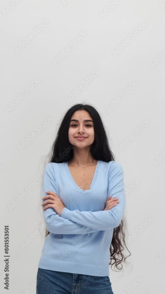 Positive portrait of a happy Indian young woman standing with crossed arms and looking at camera on white background. Vertical video. Positive portrait of a happy Indian young woman standing with crossed arms and looking at camera on white background. Vertical video.