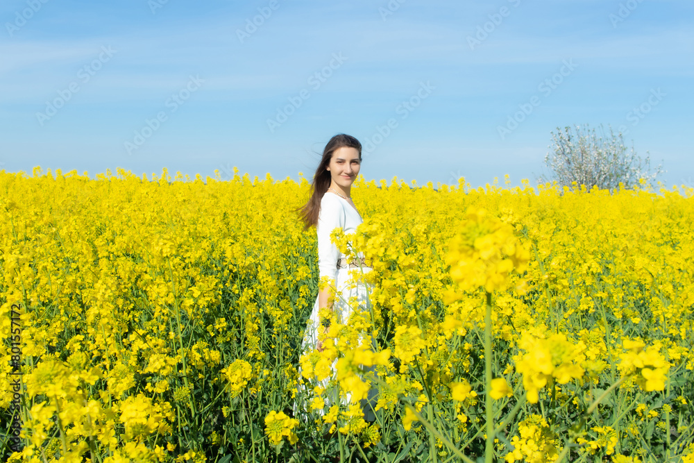 Young beautiful woman in a white dress close up in the middle of the yellow field with the radish flowers closeup on the blue sky background. Republic of Belarus, Brest region Young beautiful woman in a white dress close up in the middle of the yellow field with the radish flowers closeup on the blue sky background. Republic of Belarus, Brest region