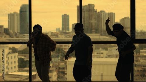Silhouette shot of skilled choreographer group dancing together with sky scrapper, cityscape background. Young hipster team dancing performance. Yellow filter. Shadow. Outdoor sport 2024. Endeavor.