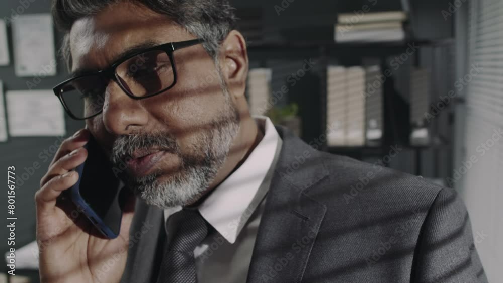 Closeup of experienced bearded Biracial executive in glasses and suit having phone conversation with business partner and discussing work issues in modern office Closeup of experienced bearded Biracial executive in glasses and suit having phone conversation with business partner and discussing work issues in modern office