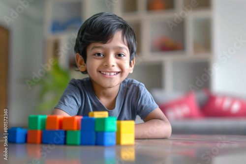 Cute indian little kid boy playing with colorful wooden, plastic blocks at home
