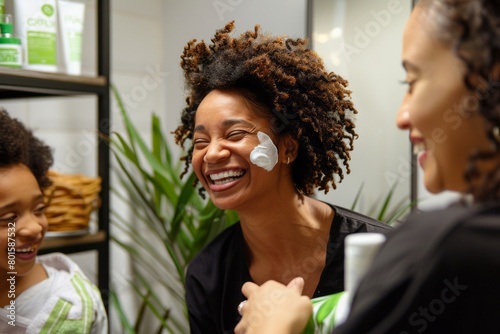 Black women are laughing and smiling, preparing for the day in the bathroom with hydrating cream photo