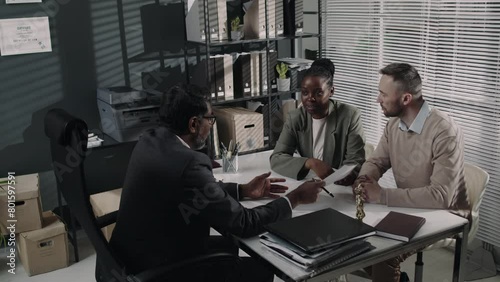Back footage of male family lawyer consulting and helping diverse couple make up prenuptial agreement before marriage during meeting at law firm photo