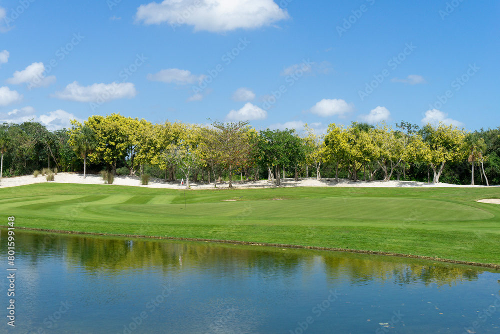 Overview of a golf course with reflecting pond, vibrant greens, fairways and tropical trees on a sunny day in Mexico. Ideal for backgrounds with copy space in the blue sky Overview of a golf course with reflecting pond, vibrant greens, fairways and tropical trees on a sunny day in Mexico. Ideal for backgrounds with copy space in the blue sky