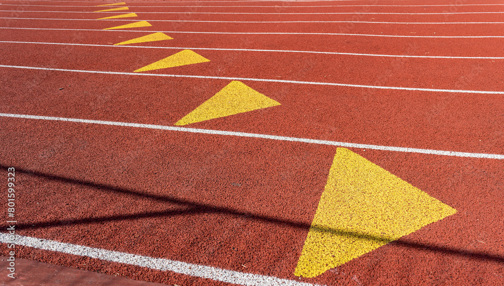 Close-up of a red athletic track with white lane marking, yellow triangles and granular texture, at an outdoor sports center in Paris