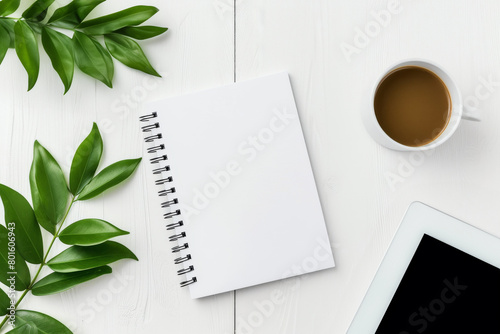 Modern workspace home office desk table with blank spiral notebook, digital tablet , cup of coffee and green plant leaves. Top view, copy space