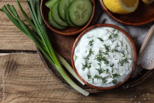 Delicious yogurt, green onion, cucumbers and dill on wooden table, top view