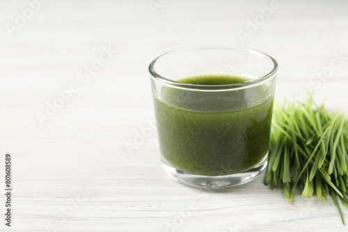 Wheat grass drink in glass and fresh sprouts on white wooden table, closeup. Space for text