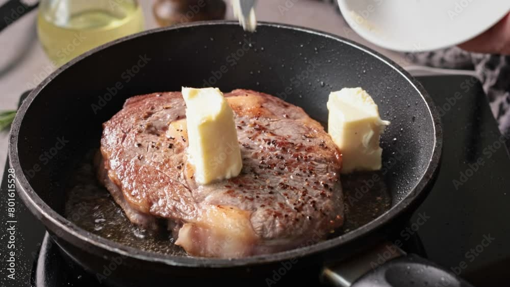 A chef adds butter, rosemary and garlic to a beef steak pan-frying in the kitchen. The process of cooking a delicious steak, close-up of the food A chef adds butter, rosemary and garlic to a beef steak pan-frying in the kitchen. The process of cooking a delicious steak, close-up of the food