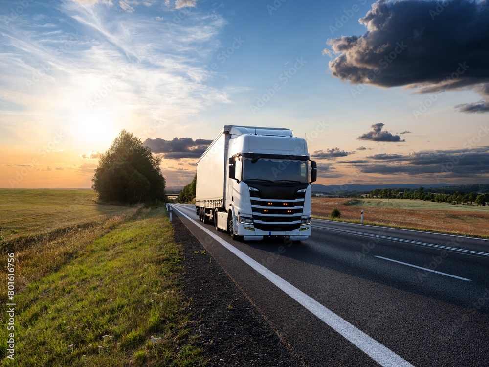 White truck driving on the asphalt road in rural landscape at sunset