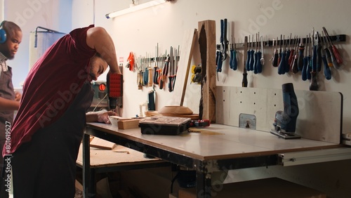 Woodworker in assembly shop using power drill to create holes for dowels in wooden board. Carpenter sinking screws into wooden surfaces with electric tool, doing precise drilling for seamless joinery photo